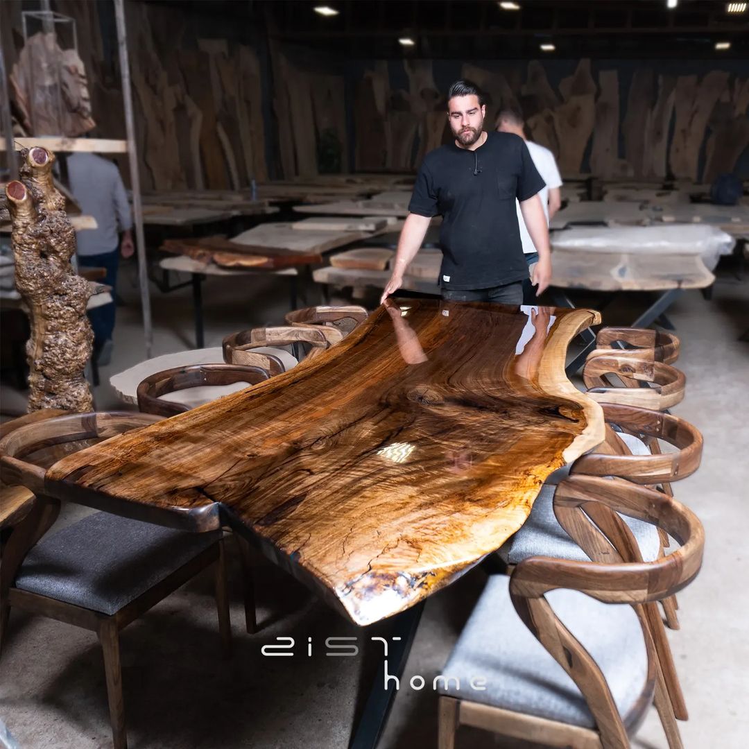 A skilled craftsman evaluating the quality of a large, natural wood slab table surrounded by stylish chairs