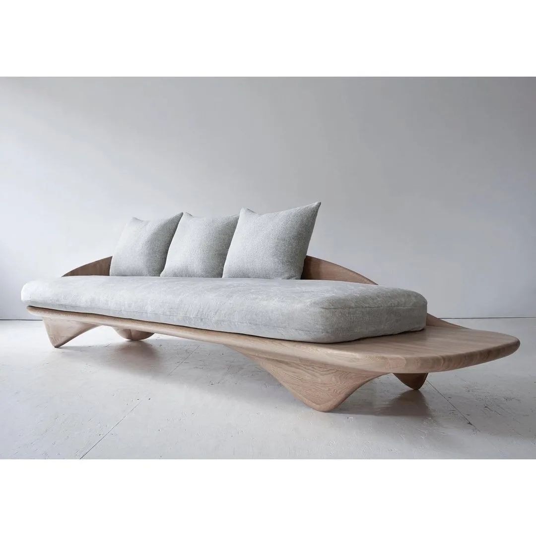 A modern and sculptural wood-framed sofa with plush grey cushioning and coordinated throw pillows