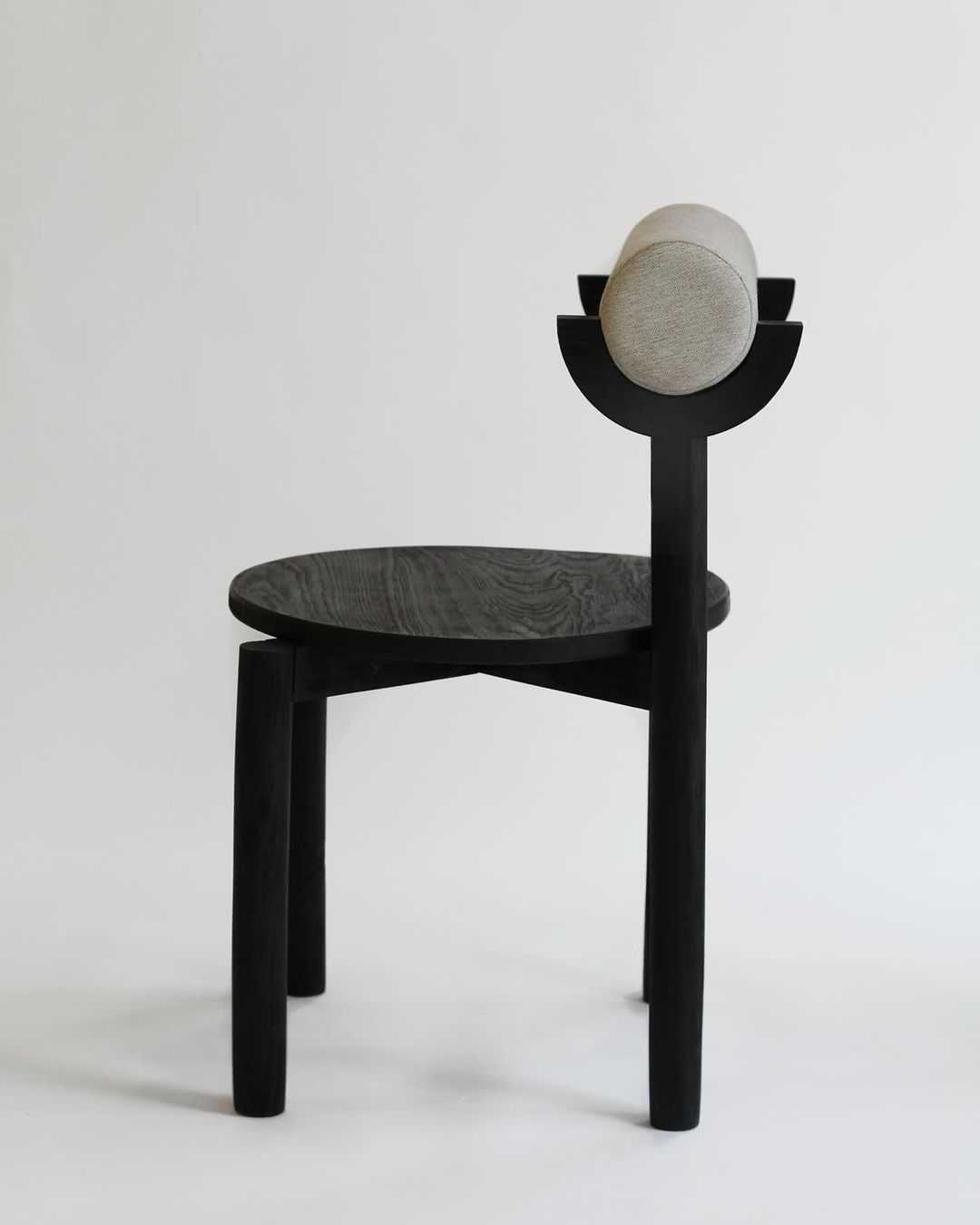 A minimalist black wooden chair with an abstract circular headrest