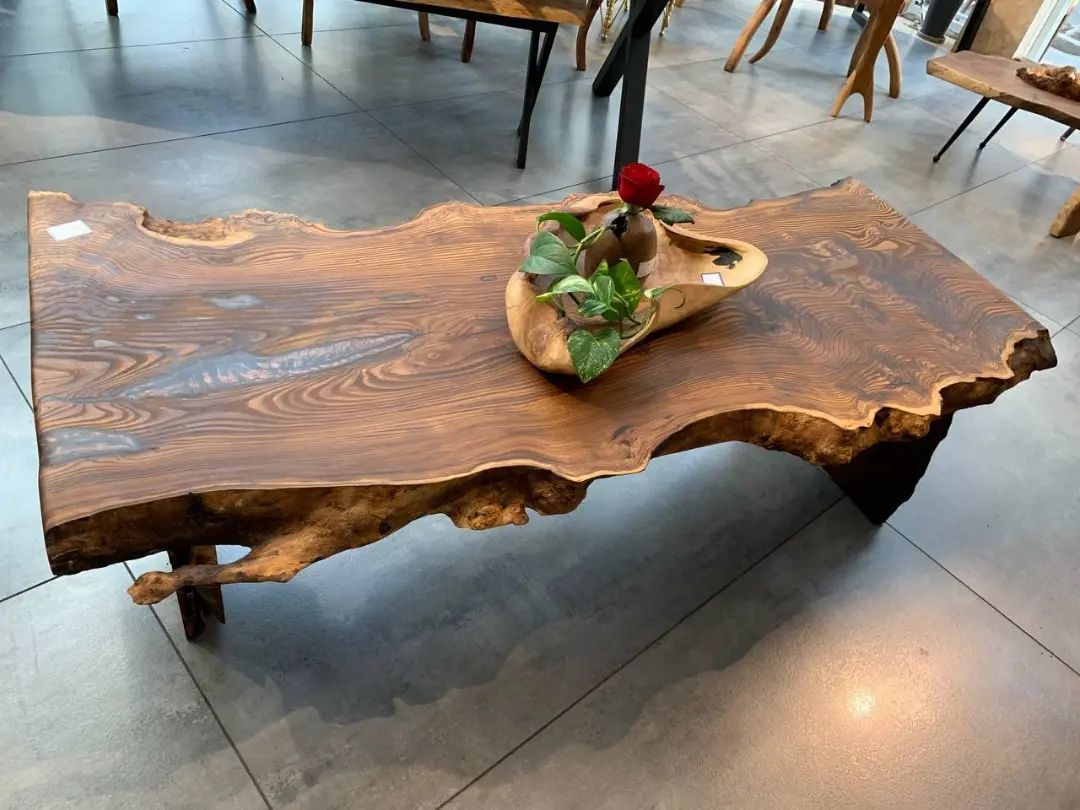 A unique wooden table with natural edges and a central cutout featuring a plant and a red flower