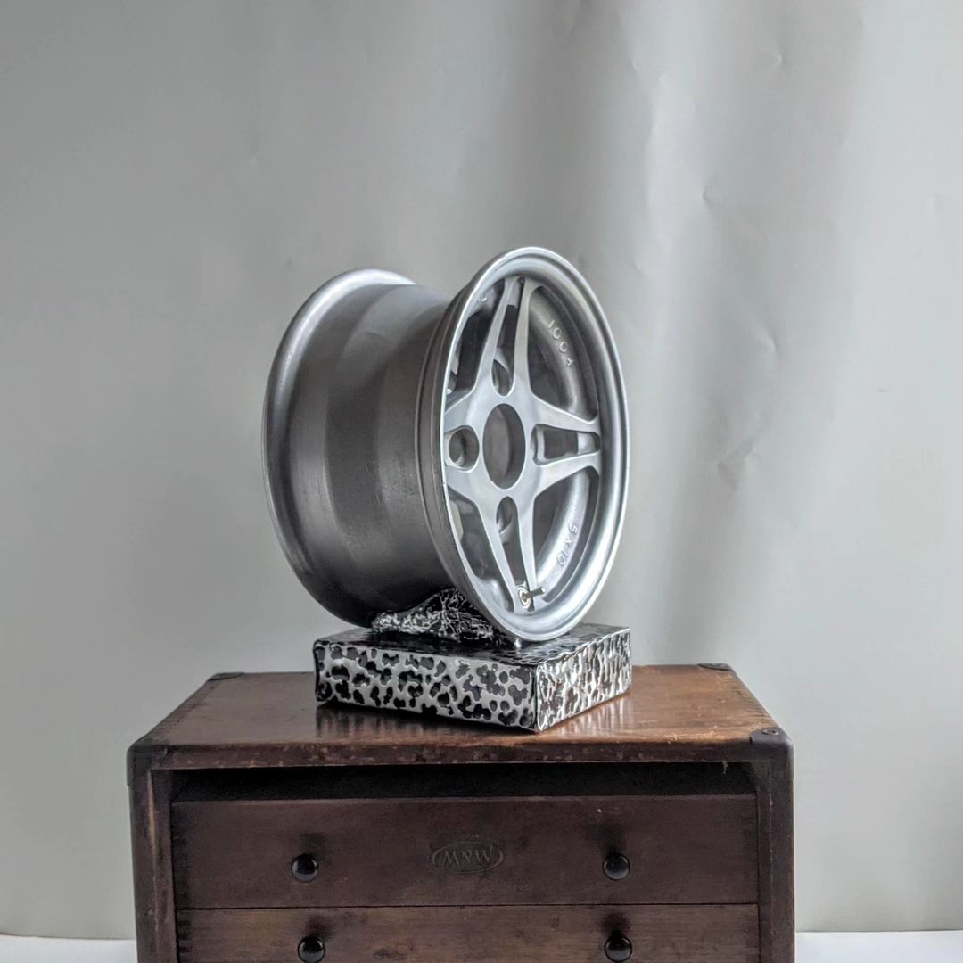 An artistic display featuring a modern car wheel resting on a leopard print stand and a rustic wooden drawer chest