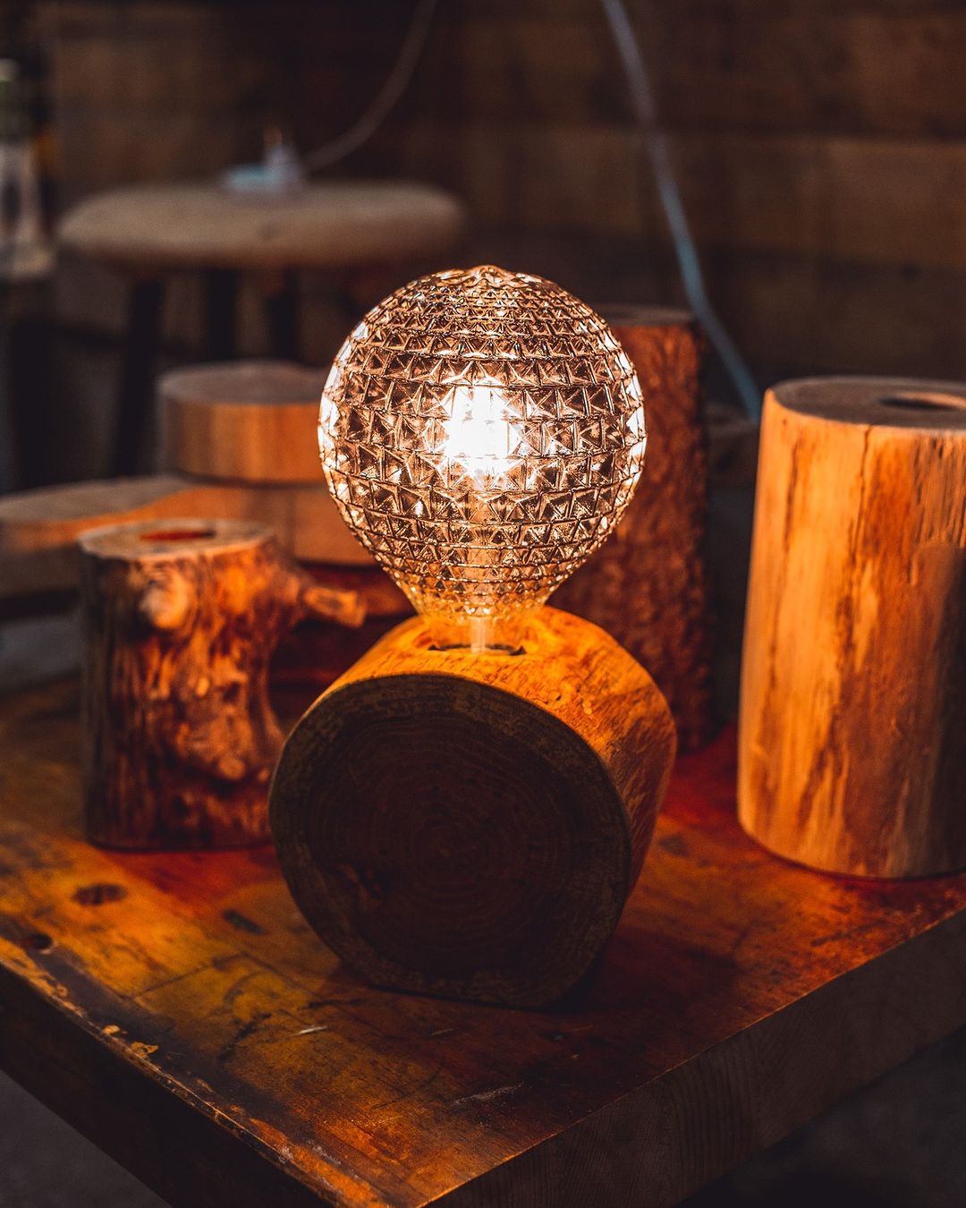 A warm and inviting table lamp with a textured glass globe atop a cylindrical wooden base emits a cozy glow, accentuating the natural wood grain.