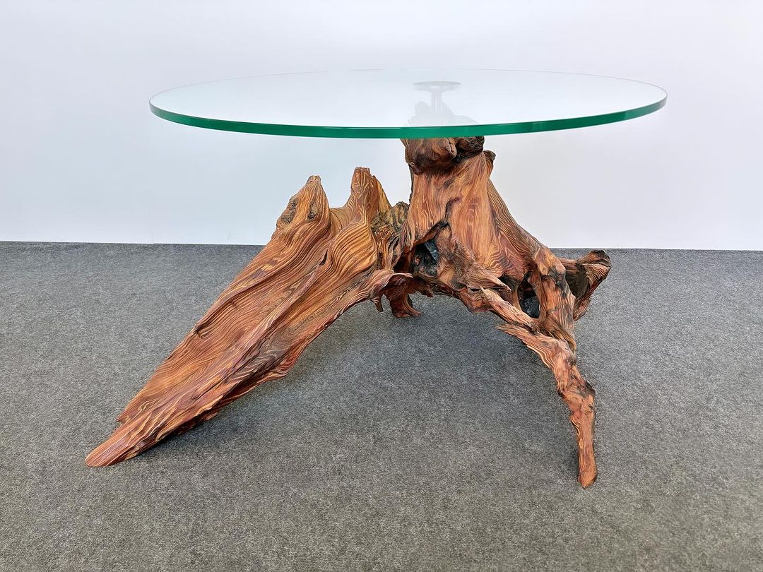 A unique table with a glass top and an organic wooden base