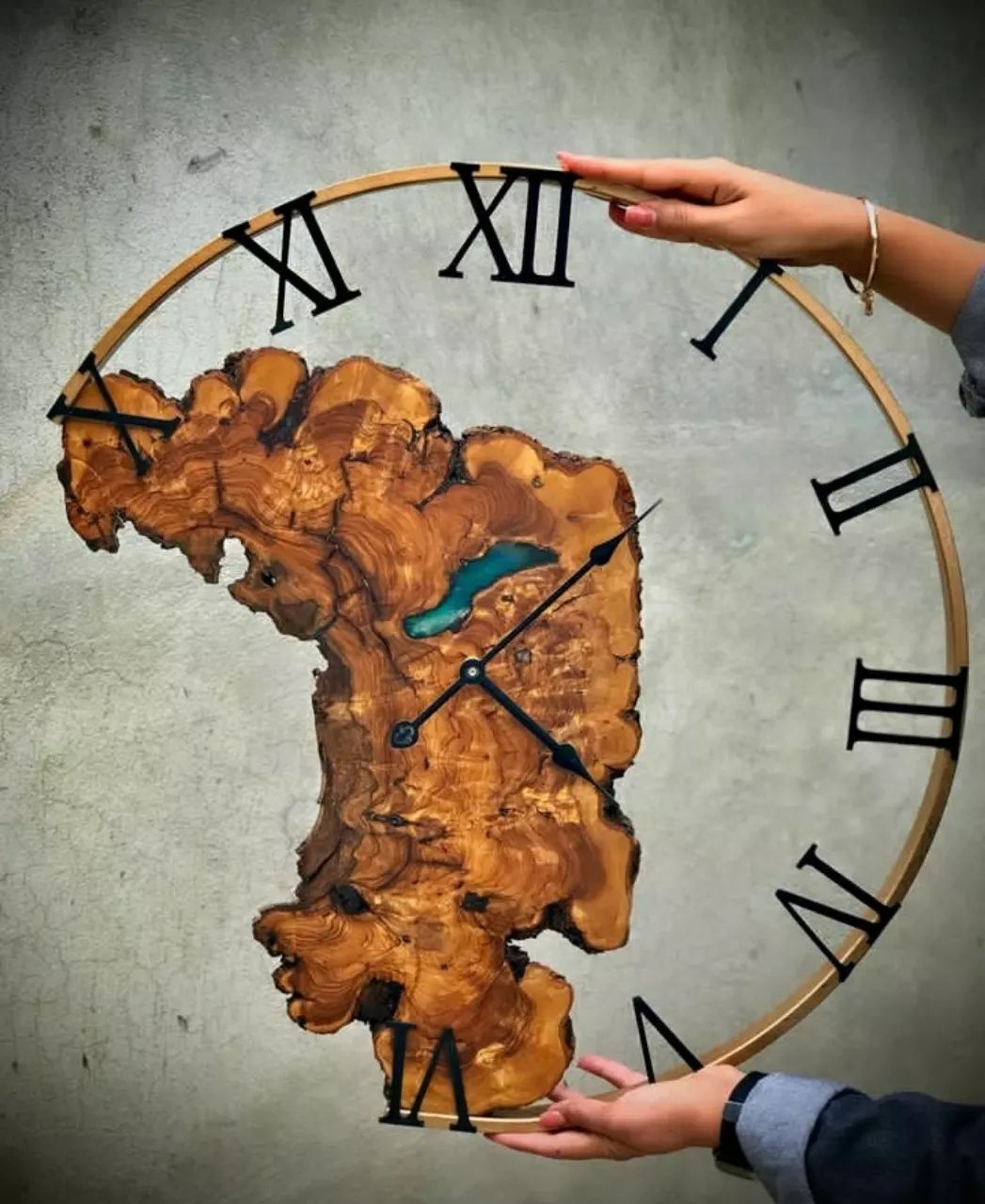 A unique wooden wall clock with resin accents, held by hands