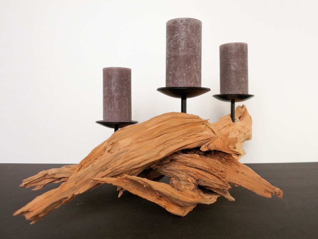 A display of three purple candles on simple black stands arranged artistically with textured driftwood for a rustic yet modern touch