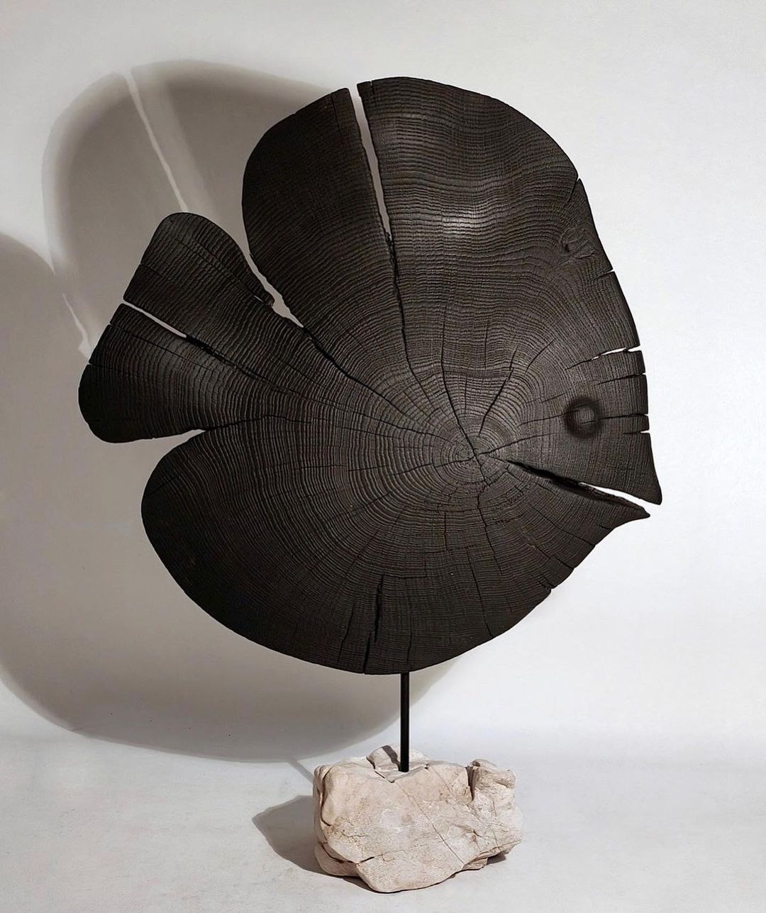 A carved wooden leaf sculpture displaying intricate rings and textures, perched on a stone base