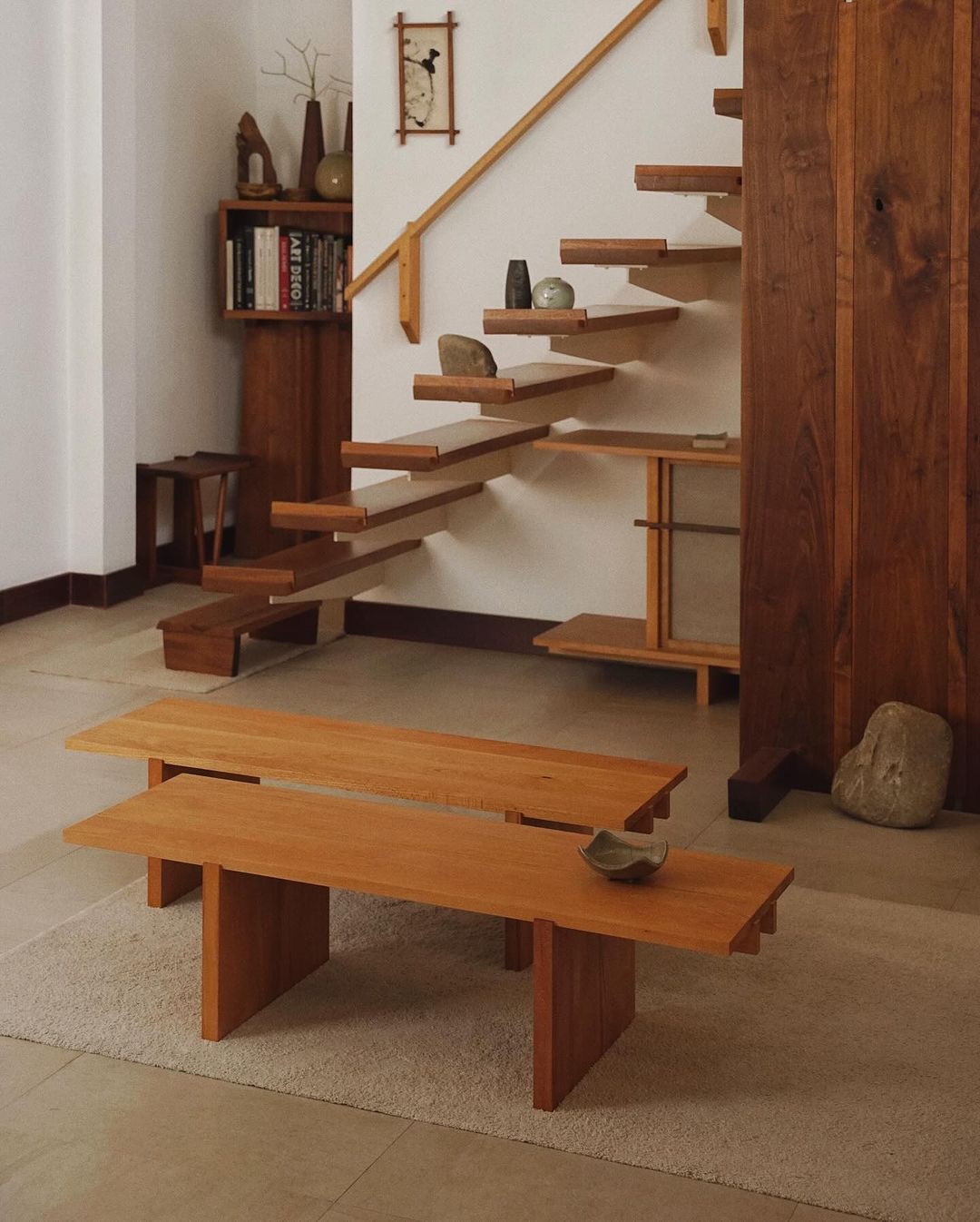 A minimalist wooden staircase ascends alongside a neutral wall, complemented by a matching simple low table and textured rug.