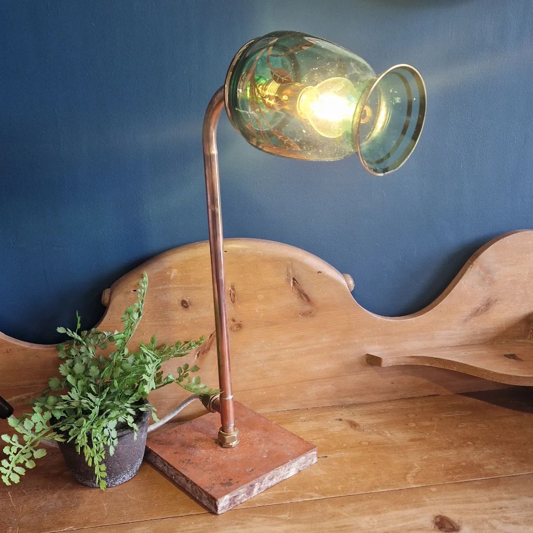 A unique desk lamp with a copper arm and a green-tinted glass shade