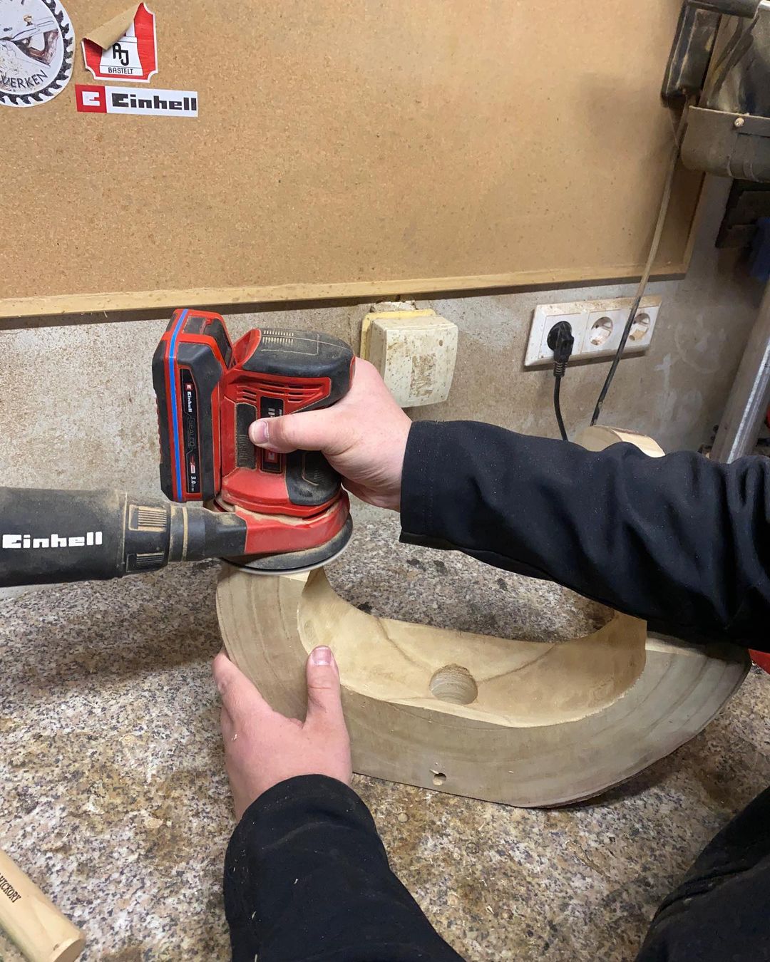 A person using a power sander to shape a wooden piece