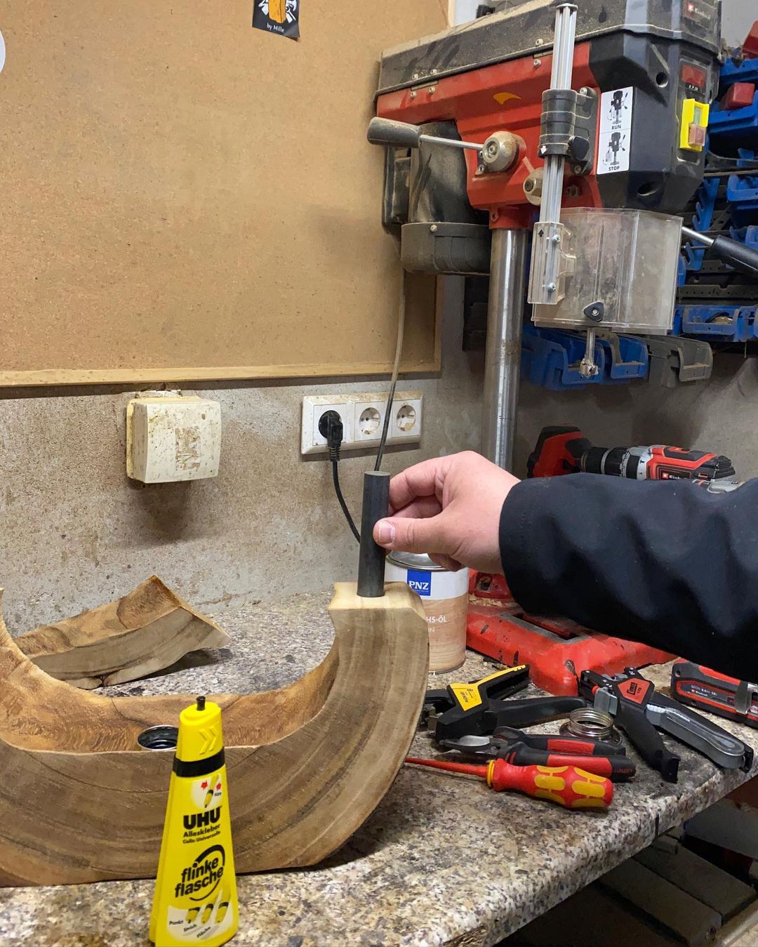 A hand carefully glues a curved wooden piece in a woodworking shop filled with various tools.