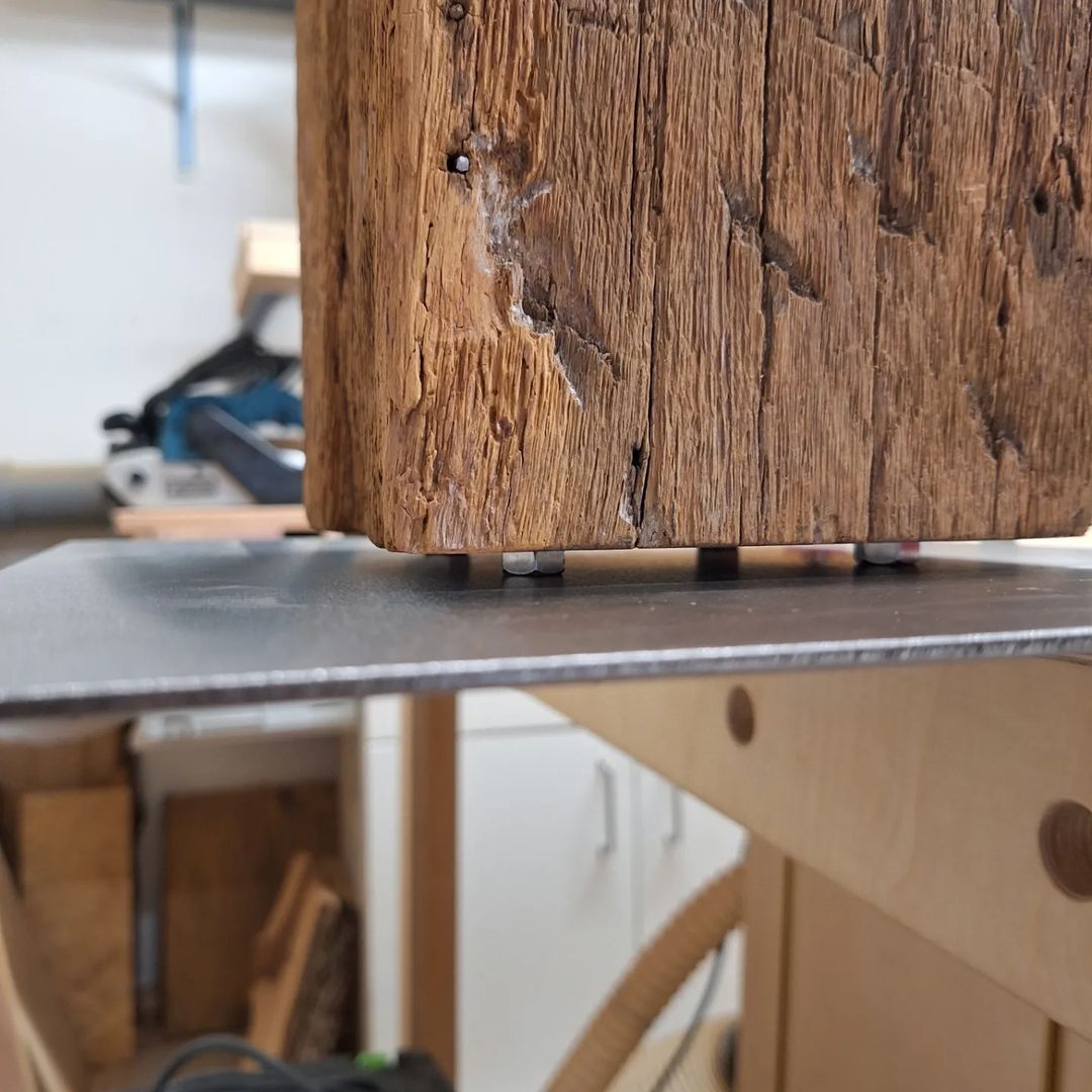 A weathered wooden beam expertly intersected by metal alignment pins on a precision table