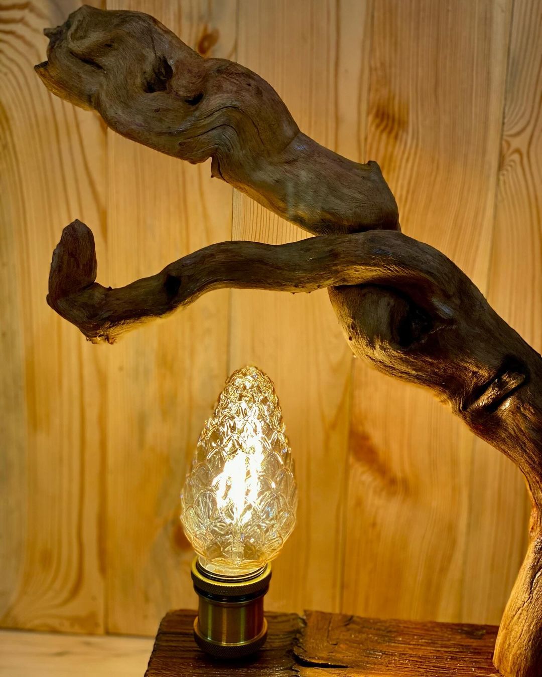 A uniquely designed lamp featuring a piece of driftwood and an illuminated textured light bulb