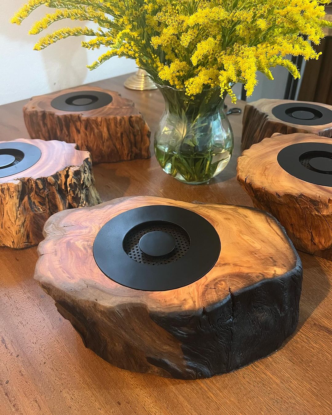 Custom wooden speakers with a natural edge finish on a table beside a vase of yellow flowers