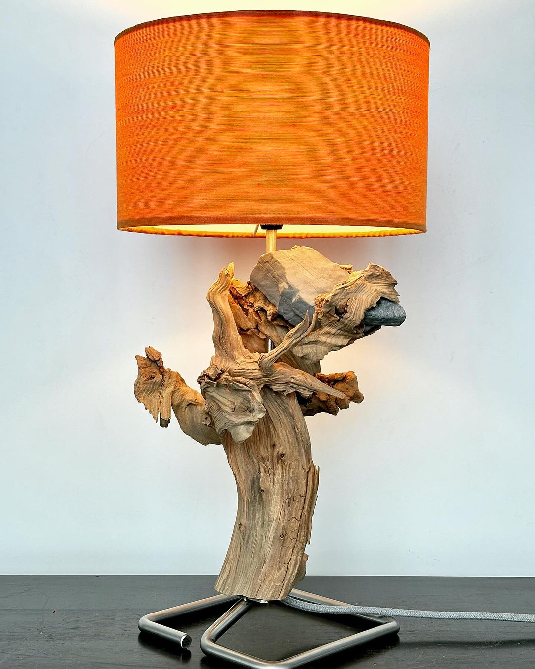 A uniquely crafted lamp featuring a driftwood base and an orange lampshade