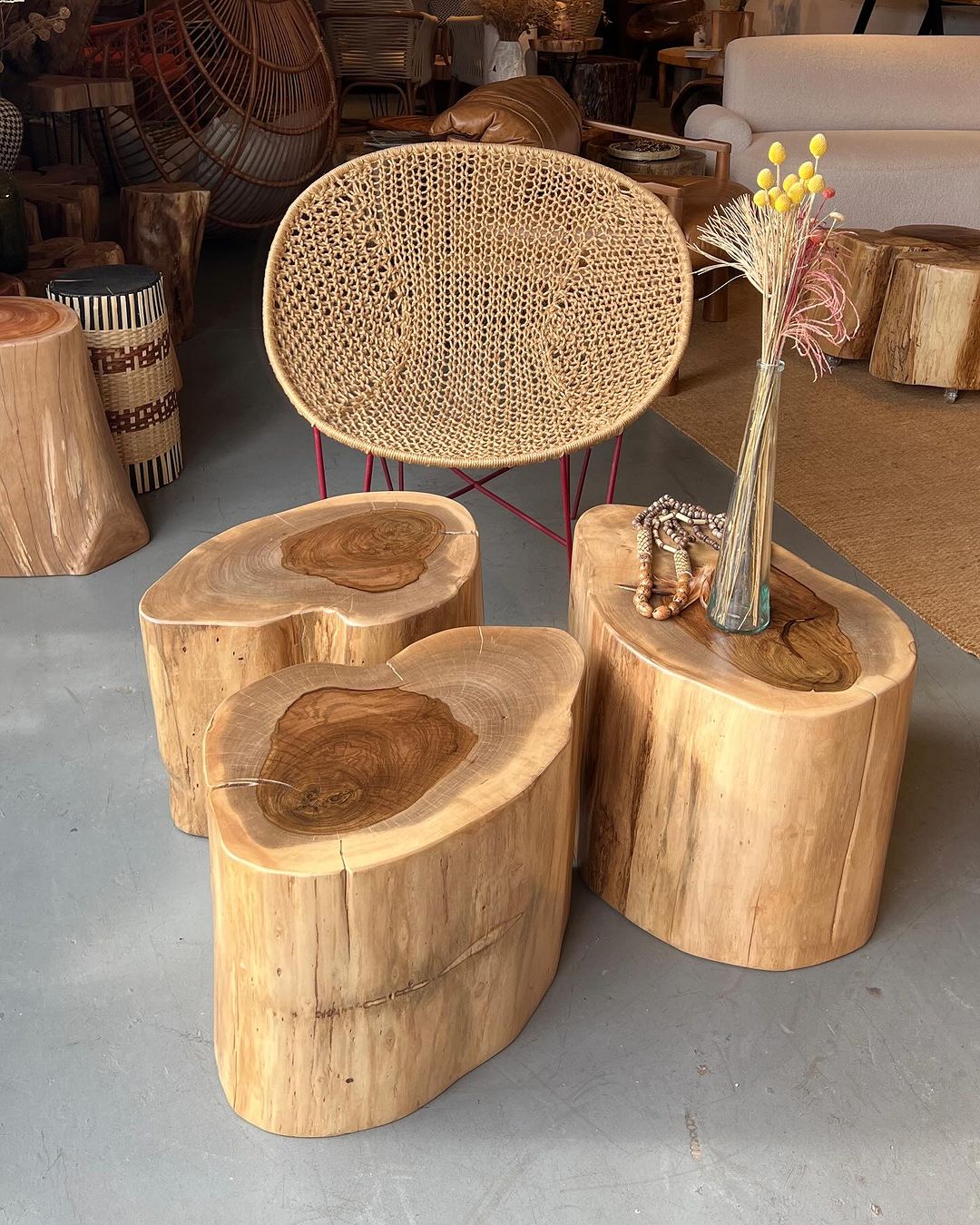 A set of four natural wood tree stump side tables and a cane webbing chair with a red steel frame.