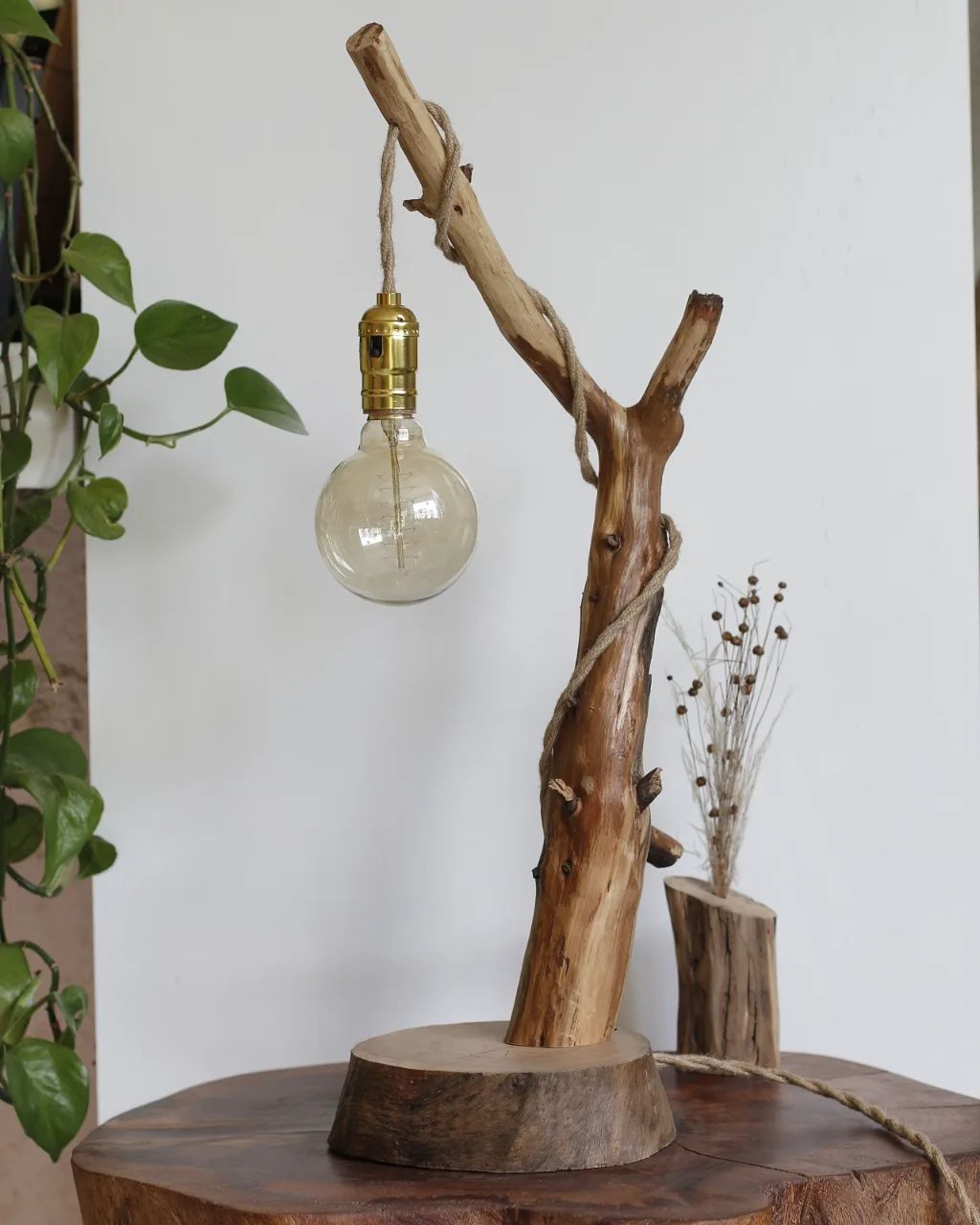 A rustic wooden table lamp with a single exposed bulb hanging from a branch