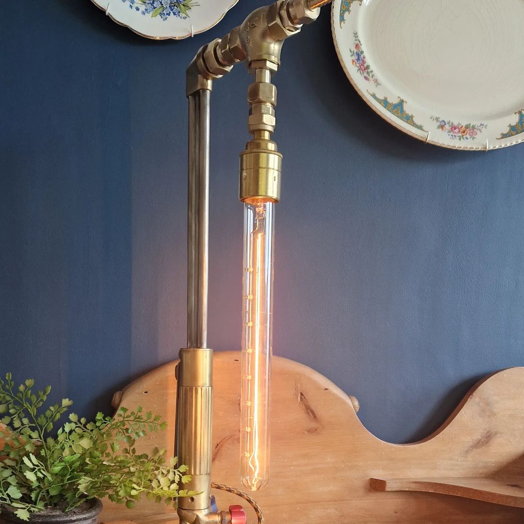 A unique, industrial-style floor lamp constructed from pipes and fittings, featuring an Edison bulb