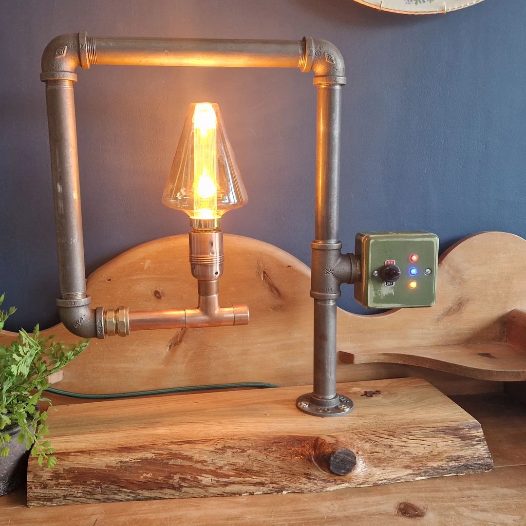 A uniquely crafted lamp made from industrial pipes with an Edison bulb, mounted on a rugged wooden base.