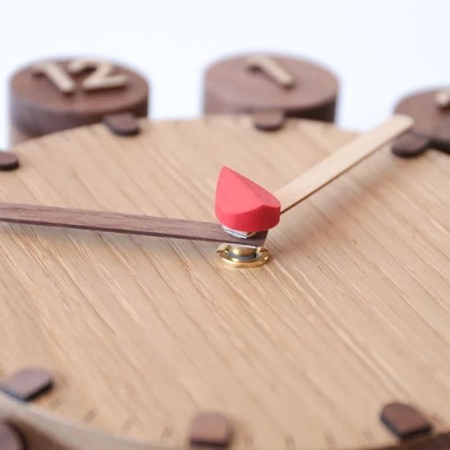 A precisely balanced miniature red seesaw on a wood surface with geometric shapes