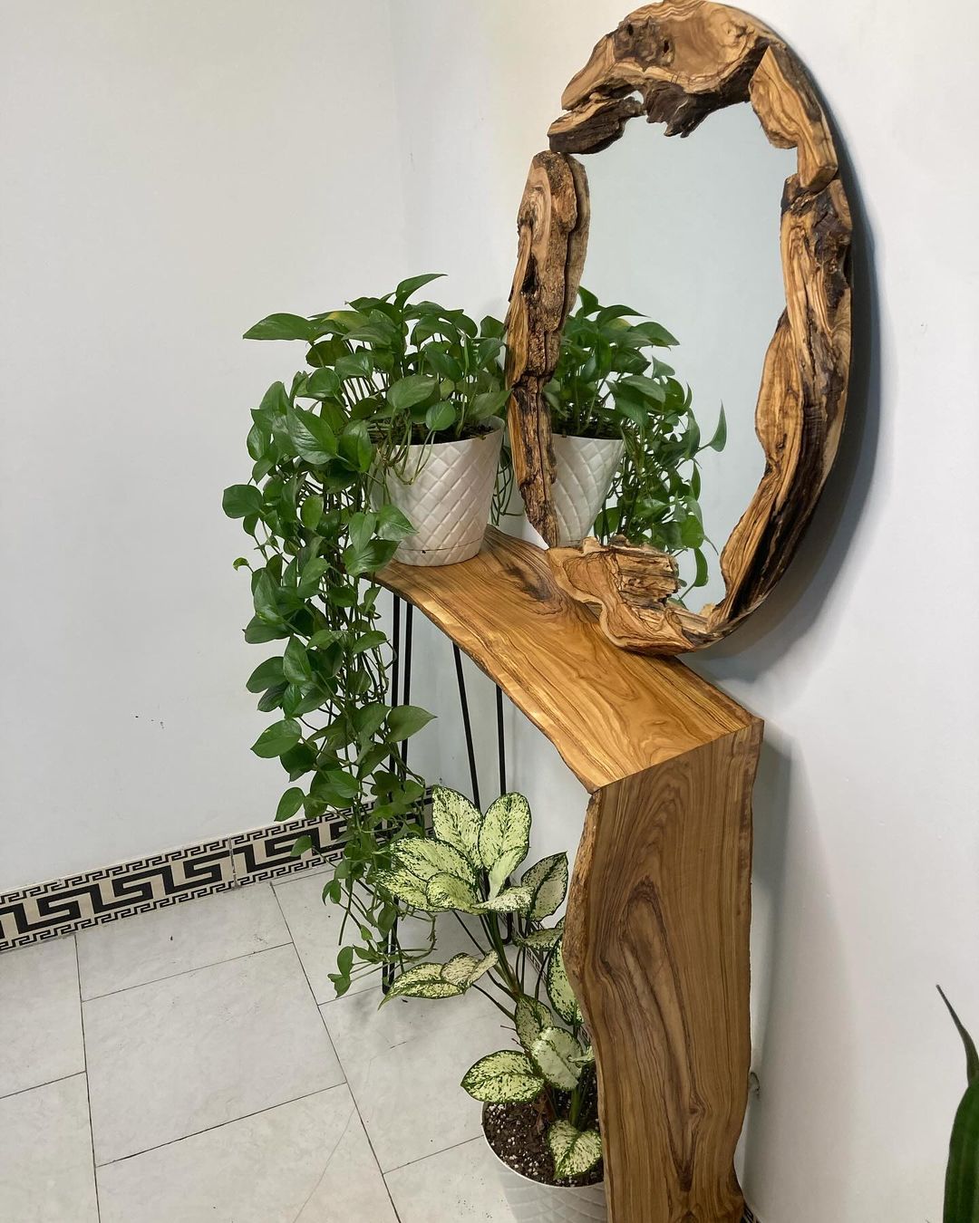 A chic interior corner featuring lush green plants arranged on a wooden console with an artistic mirror