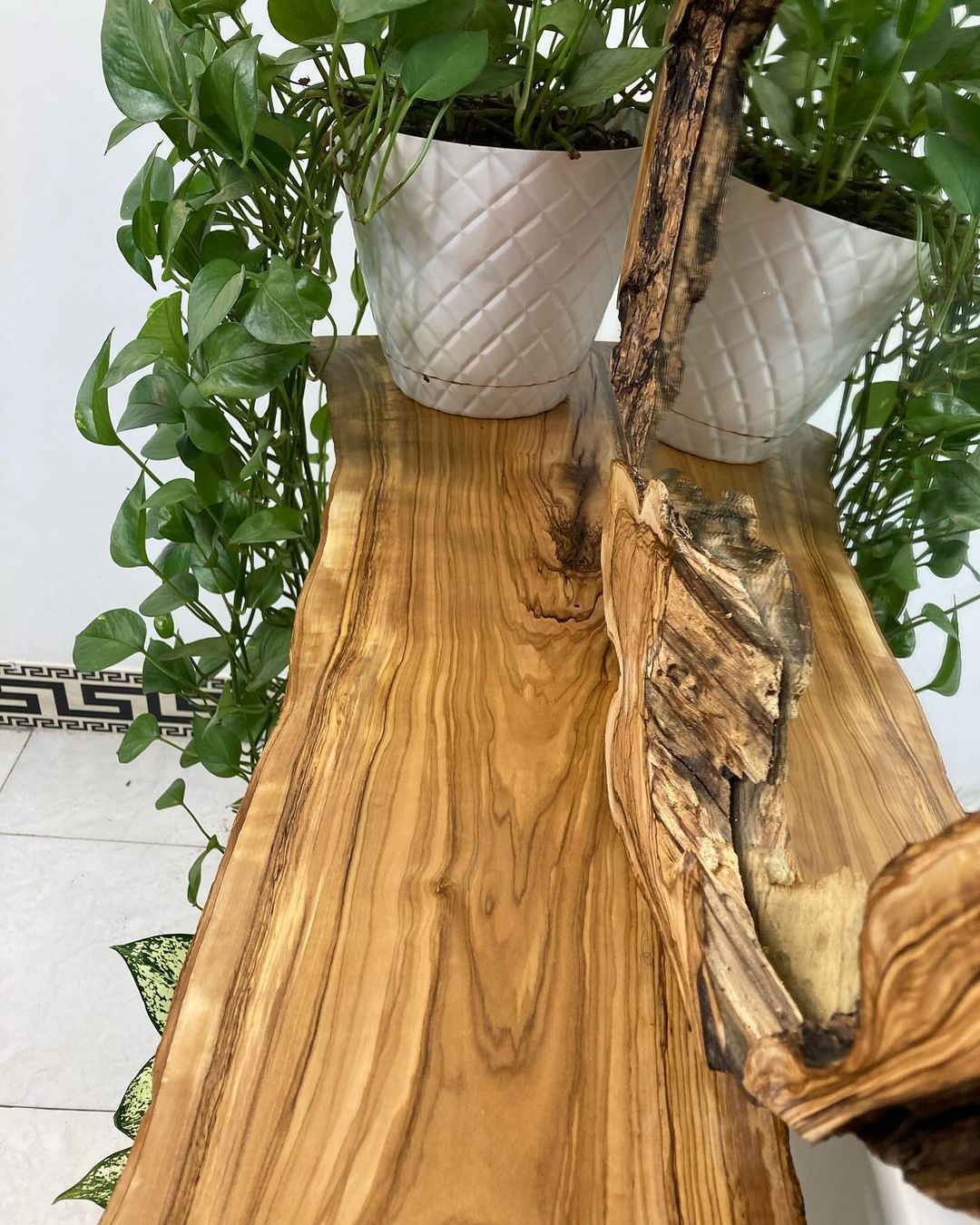 A handcrafted wooden console table featuring a vibrant plant in a white textured pot.