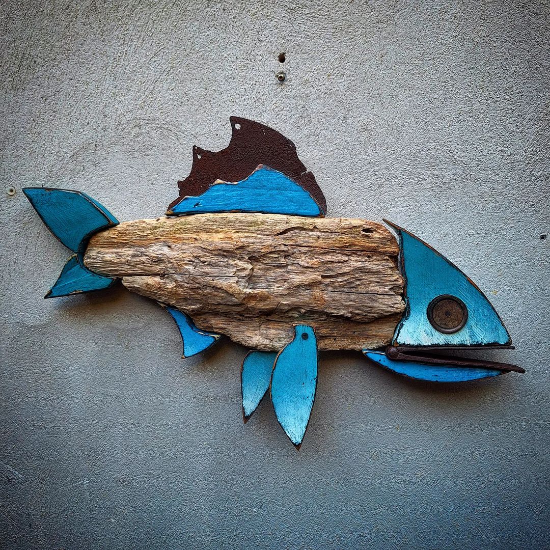 A piece of wall art depicting a fish crafted from a combination of driftwood and painted wooden elements