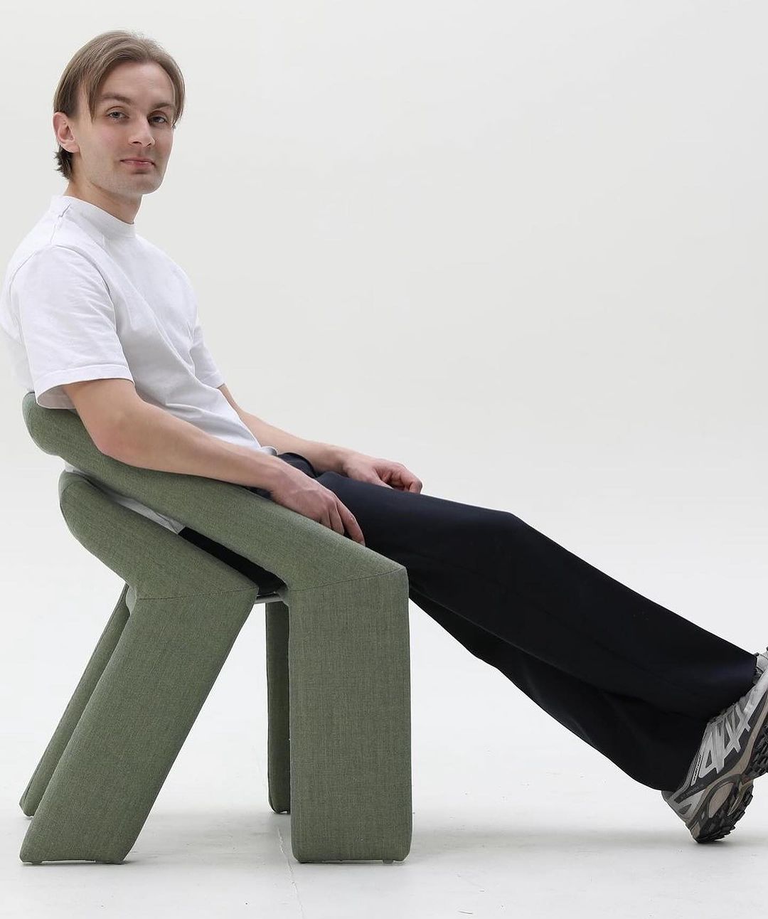 A man sitting on a uniquely structured green chair with elongated leg rests