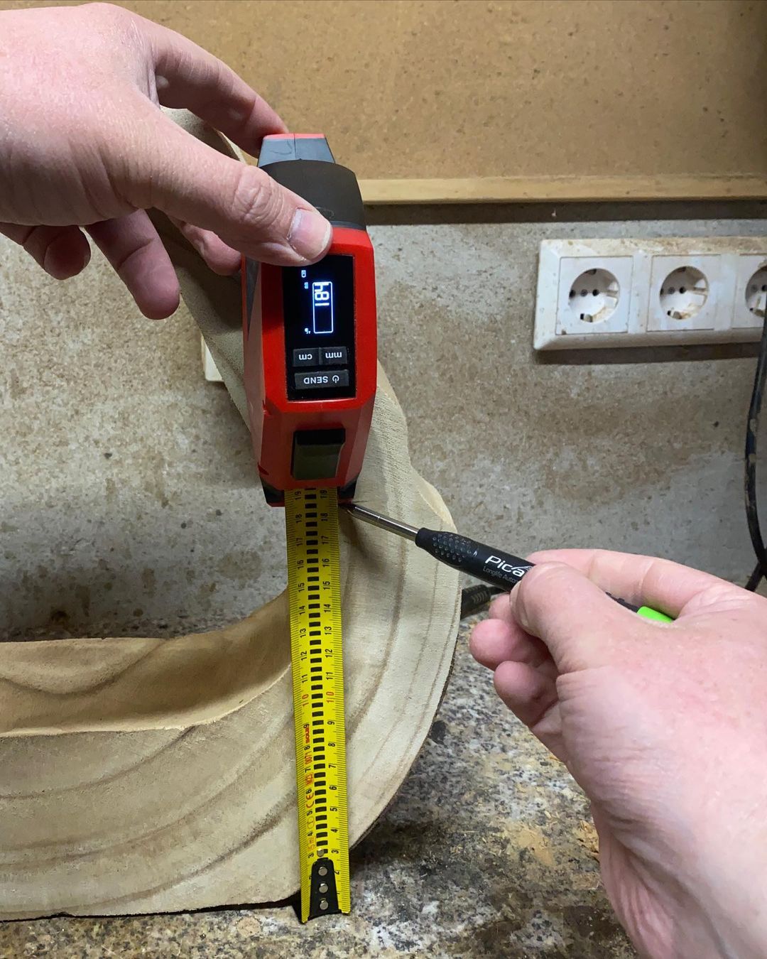 A person using a digital laser measuring device to measure the distance to a tape measure