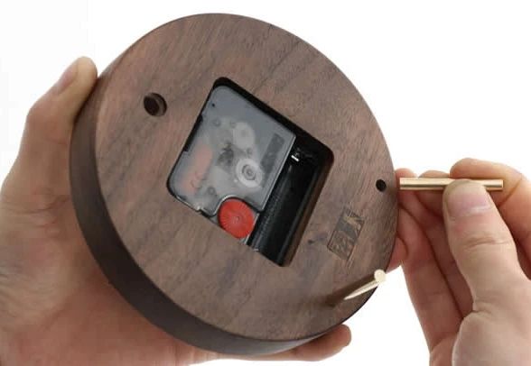 A hand winding a mechanical wooden clock