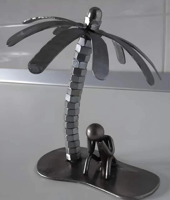 An artistic metal sculpture depicting a scene with a palm tree and a seated figure beneath it