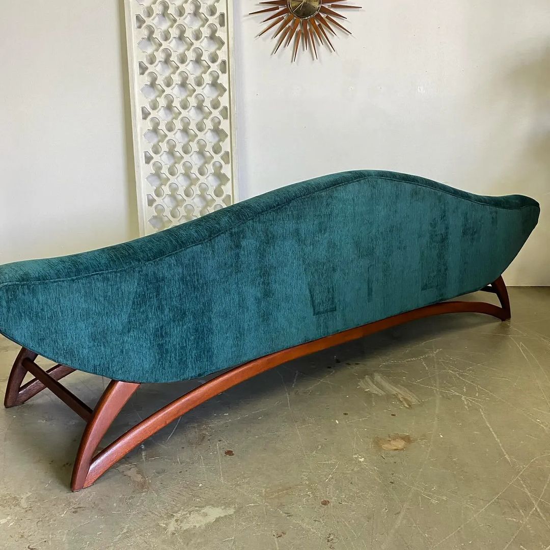 A unique teal blue mid-century modern chaise lounge with a curved silhouette and wooden legs.