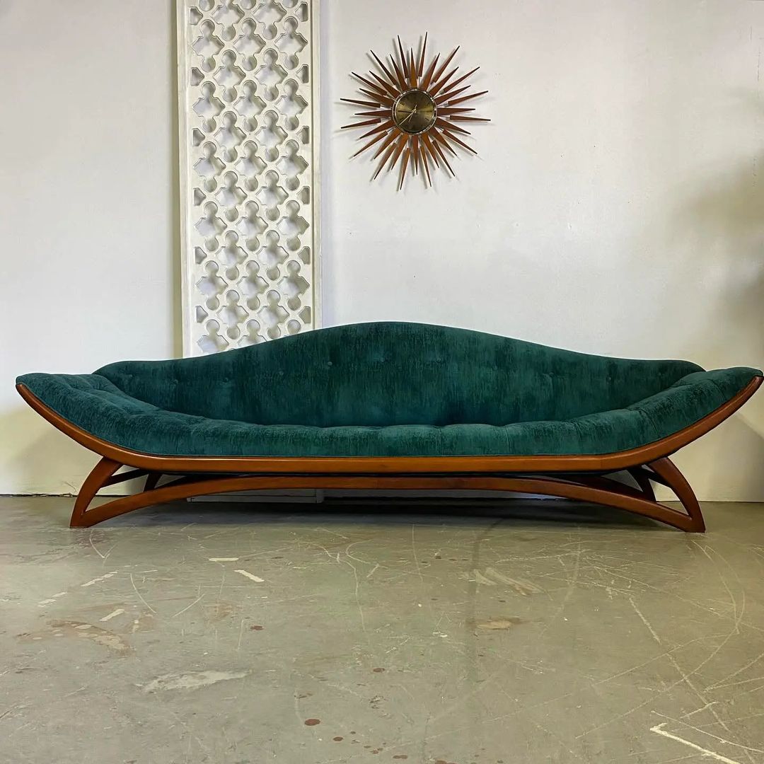 A uniquely curved teal velvet couch set upon a sleek wooden base for a touch of mid-century modern elegance in interior design.