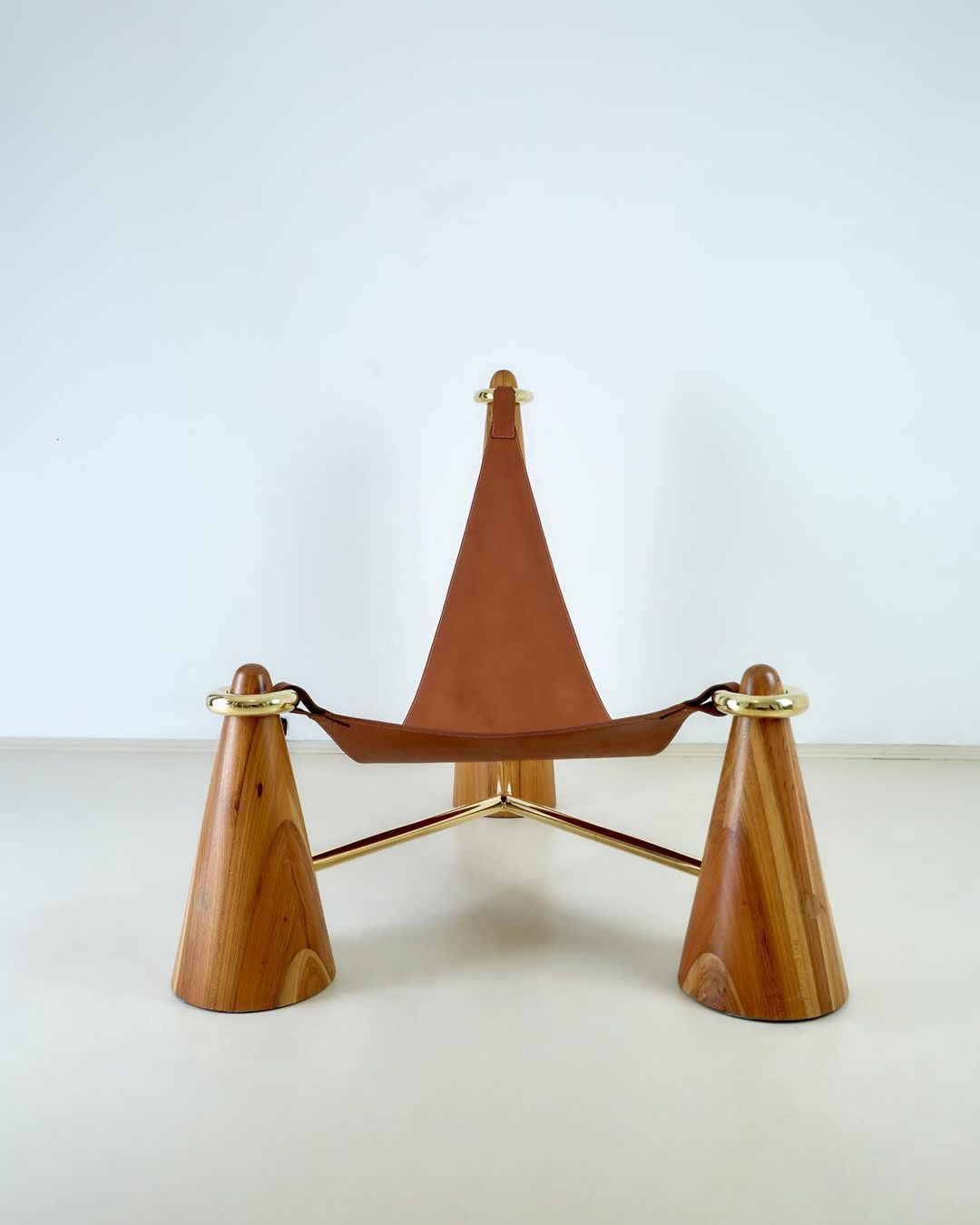 A unique mid-century tripod leather stool with wooden legs and brass accents