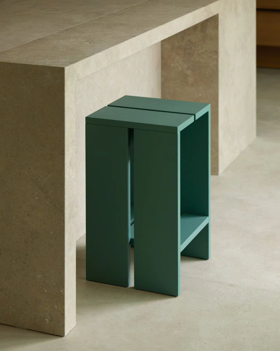 A dark green minimalistic stool tucked neatly under a concrete table