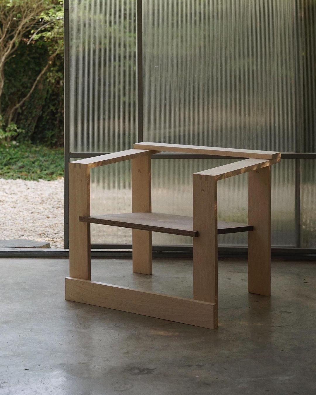 An intentionally minimalist wooden chair with a single lower shelf