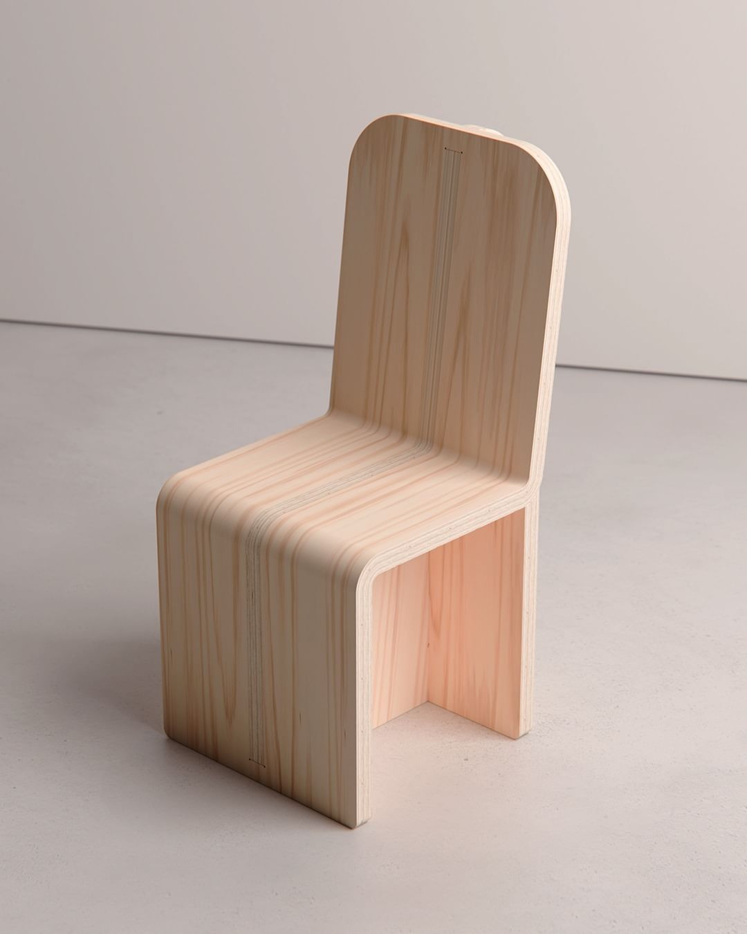 A minimalist wooden chair with a curved backrest and seamless design