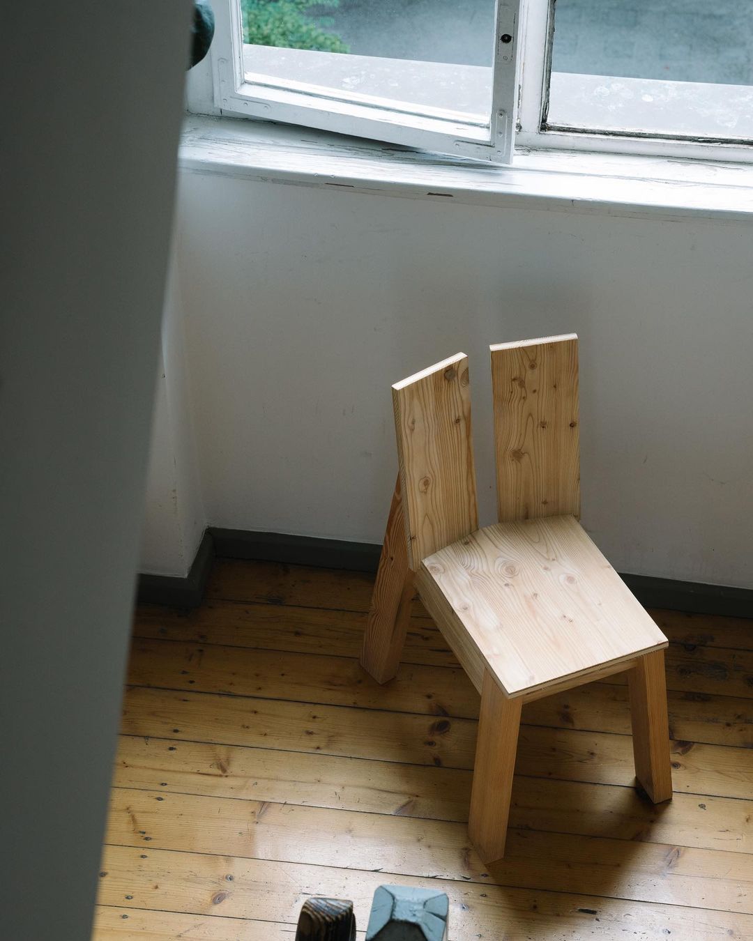 A minimalist wooden chair placed in a corner by a window, providing a serene spot for contemplation.