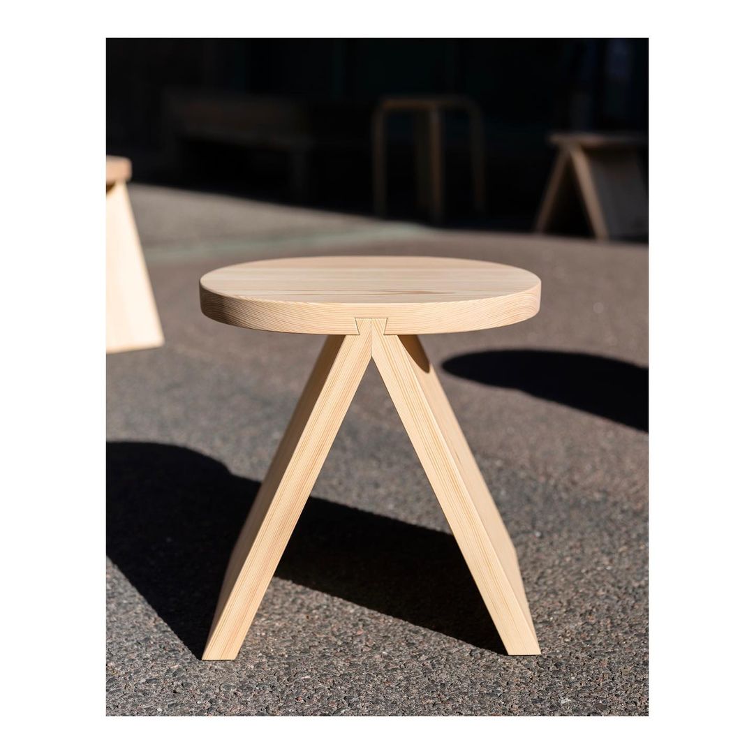 A minimalist wooden stool with a round top and angled legs