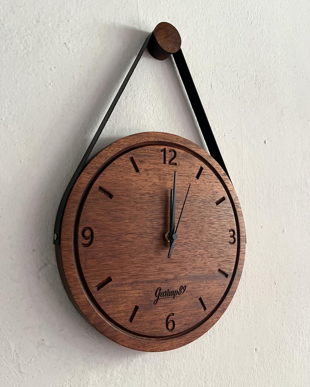 A minimalist wooden wall clock with a triangular hanging element