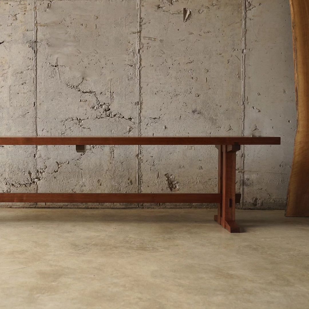 A minimalistic wooden bench against a textured concrete wall