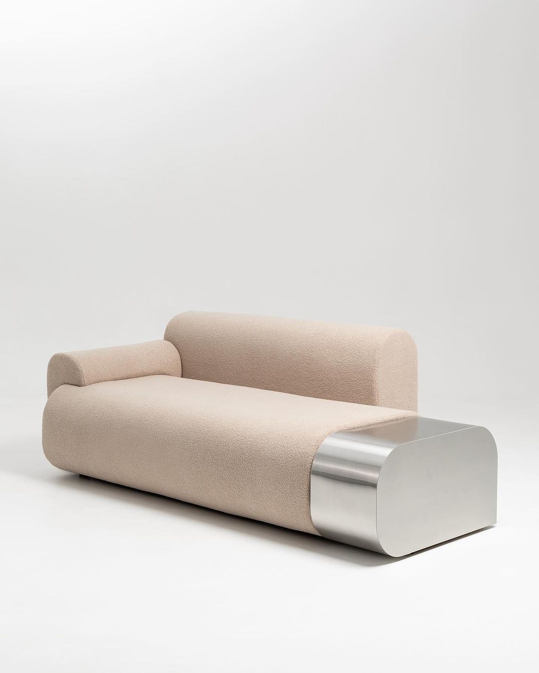 A unique and modern sofa with a beige boucle upholstery and a polished stainless steel base