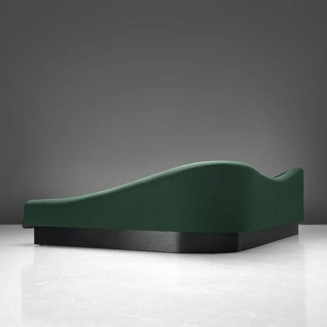 A minimalist chaise lounge with a sleek silhouette and forest green upholstery