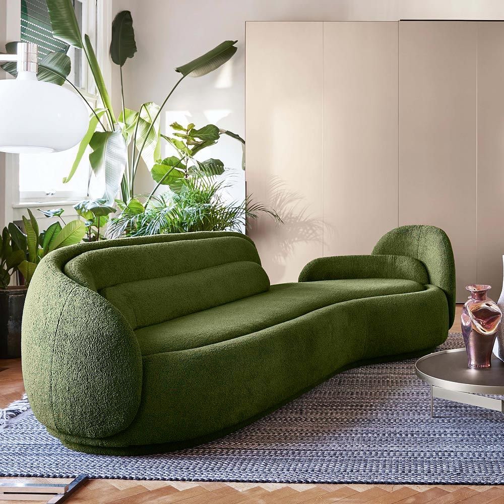 A vibrant green textured sofa with rounded edges, set within a stylish, well-lit space with indoor plants and minimalist decor.