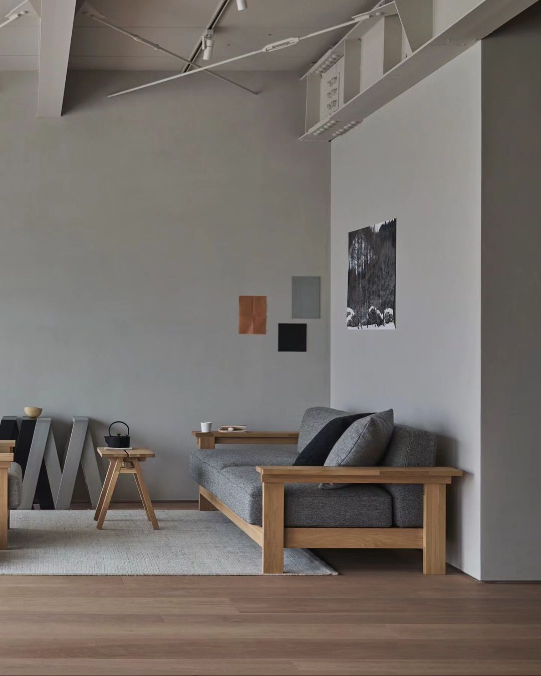 A modern, minimalist living room featuring a wooden-framed charcoal sofa, paired with a simple wood coffee table on a textured rug