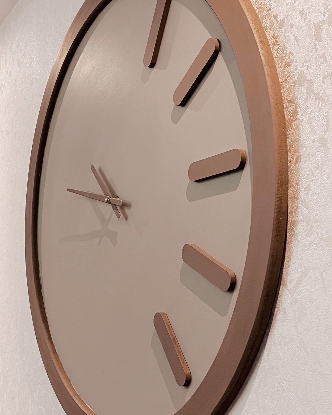 A modern wall clock featuring a minimalist design with oversized wooden hour markers on a grey backdrop.