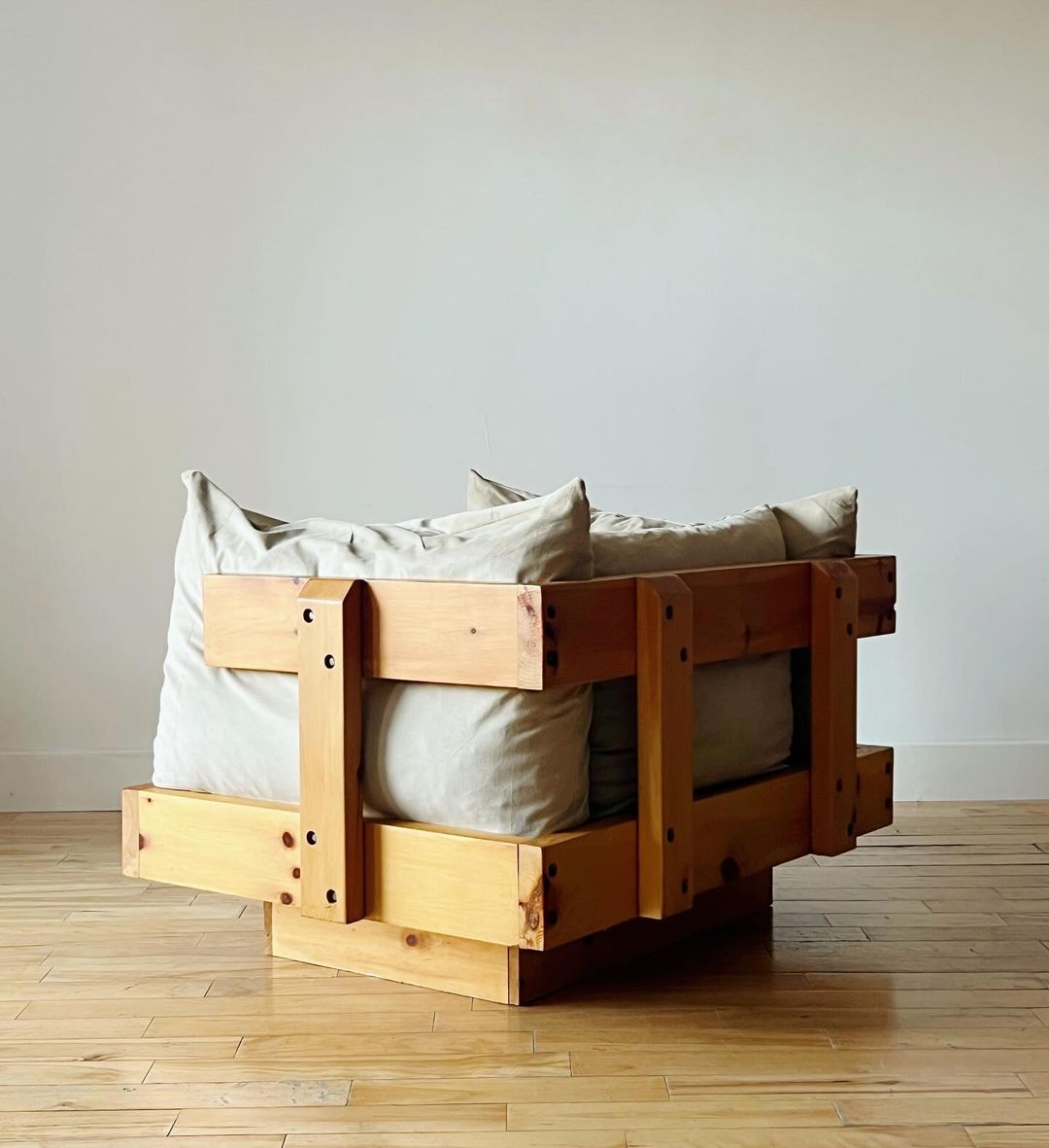 A modern, minimalist armchair crafted from wooden pallets, featuring plush neutral-toned cushions