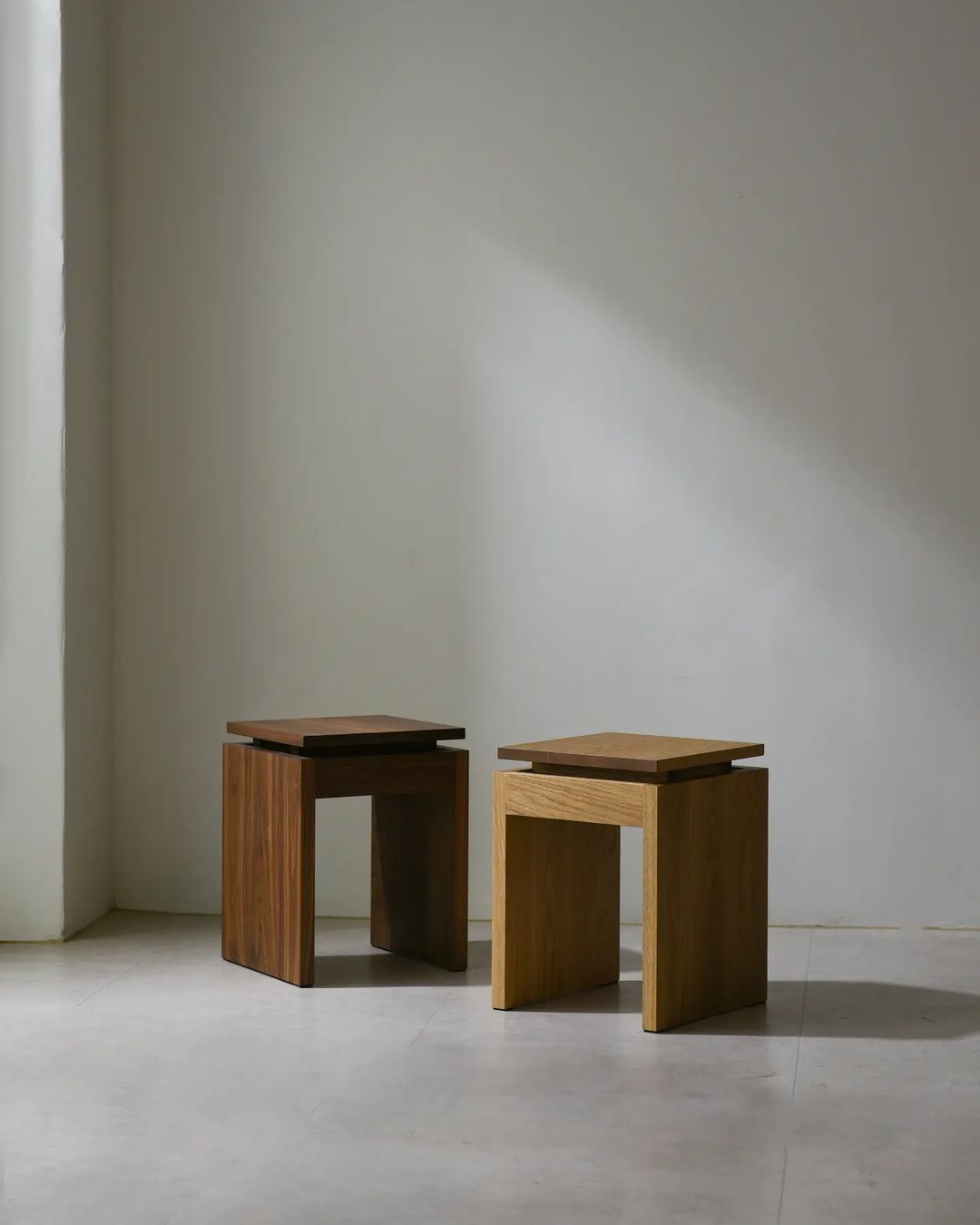 Two wooden stools of different shades against a bare wall