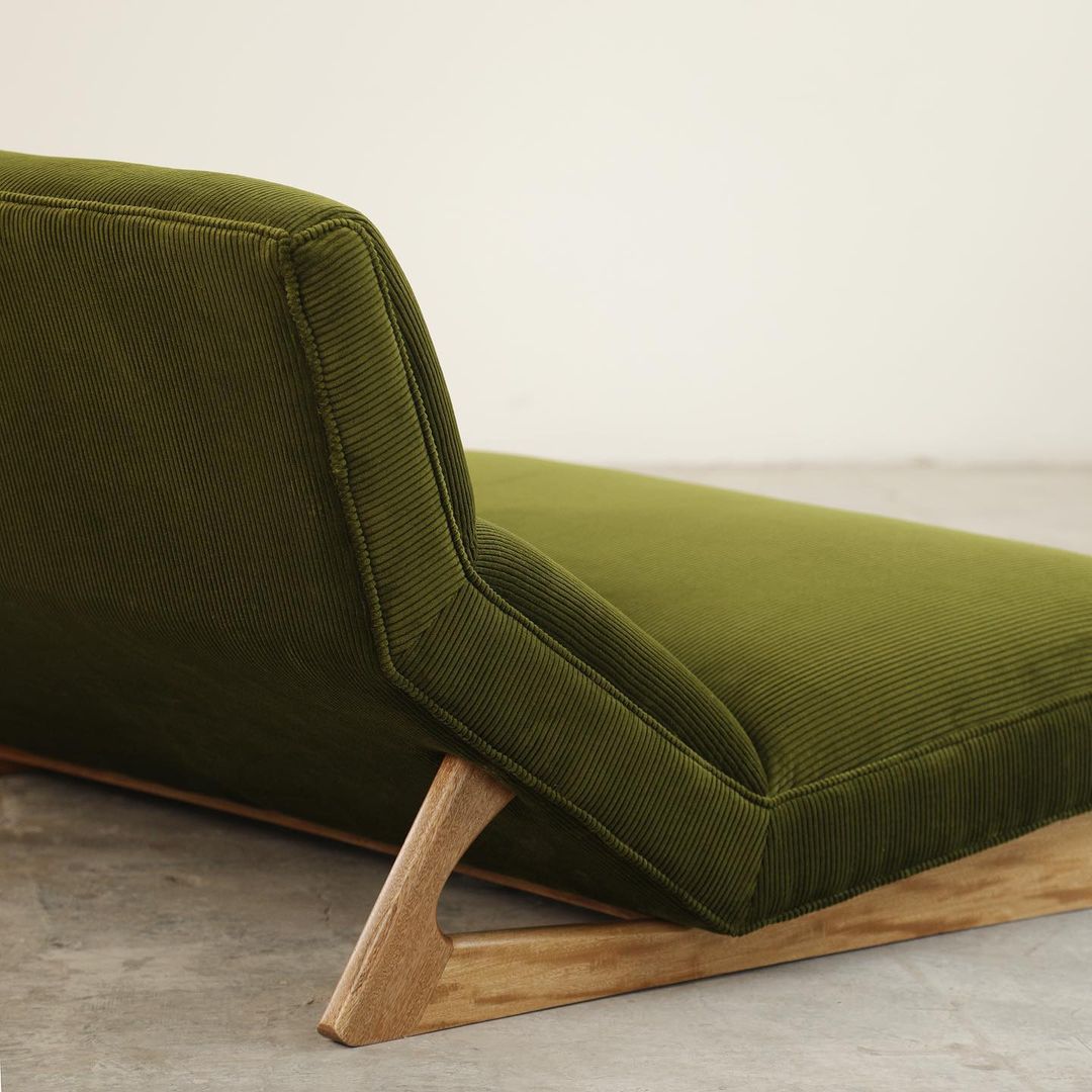 A modern olive green daybed with corduroy upholstery and sleek wooden legs.