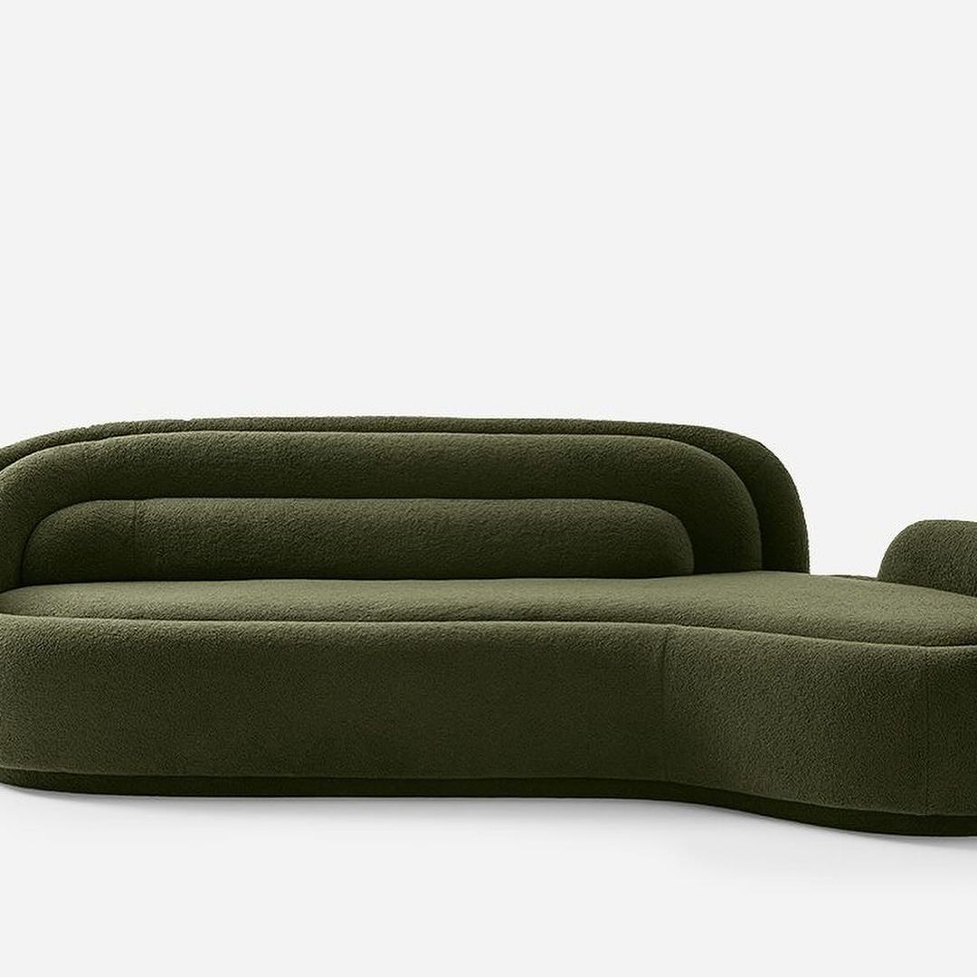 A plush, olive green sofa with gracefully curved lines and a chaise lounge component