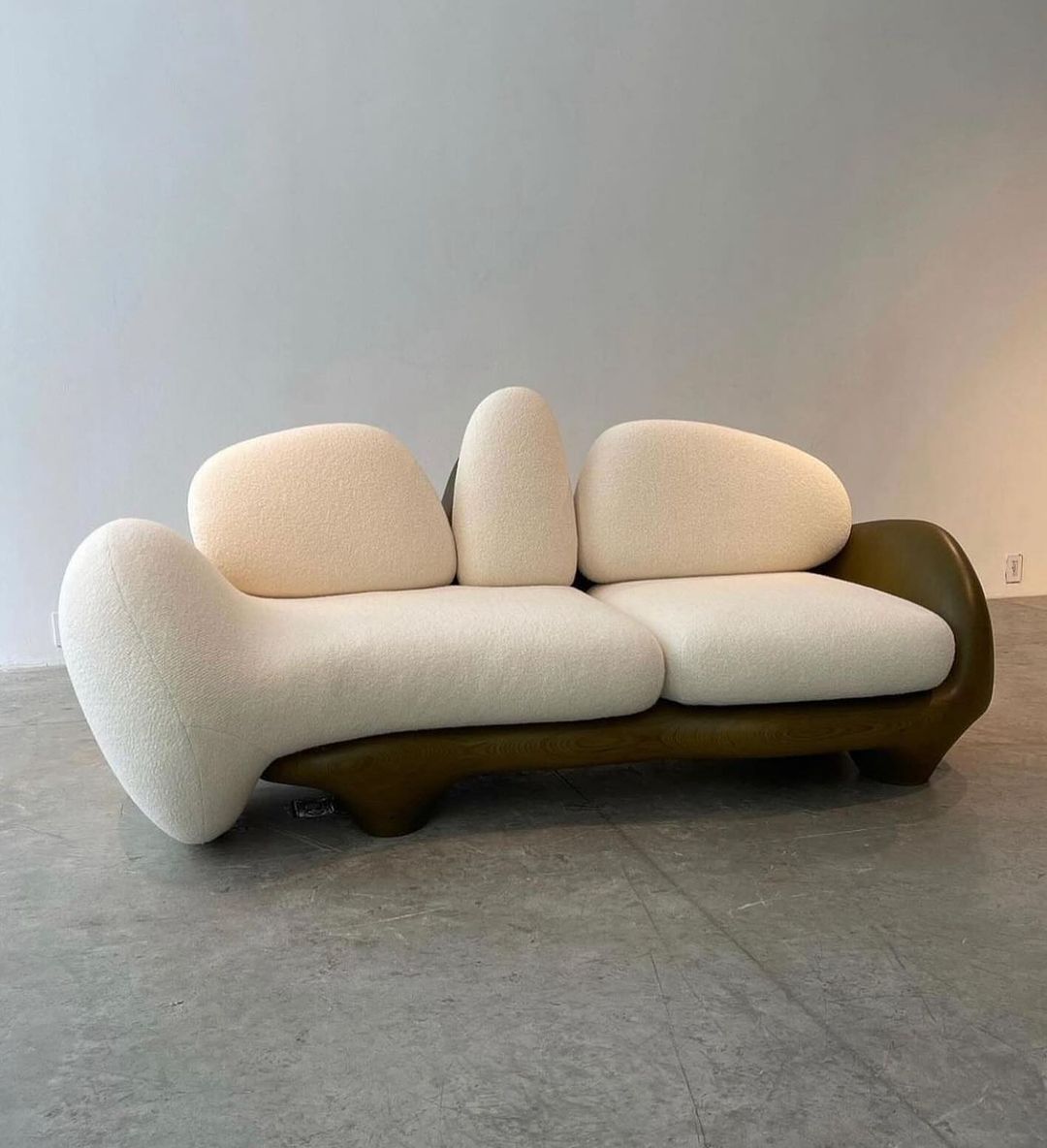 A uniquely sculptural modern sofa with voluptuous cushions and a curvy wooden base